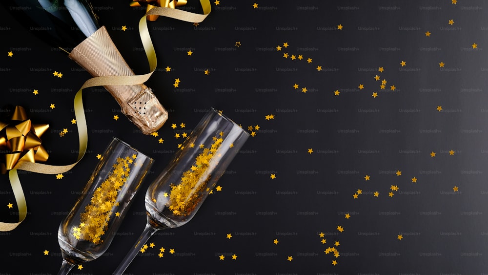 Christmas champagne bottle and glasses with golden confetti and decorations on black background. Flat lay, top view, copy space. Banner mockup, greeting card template.