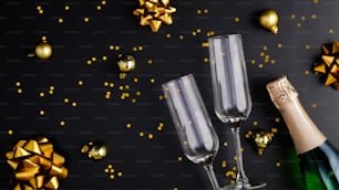 Fondo navideño de lujo negro con botella de vino, copas de champán, decoraciones navideñas brillantes y confeti dorado. Plano, vista superior.