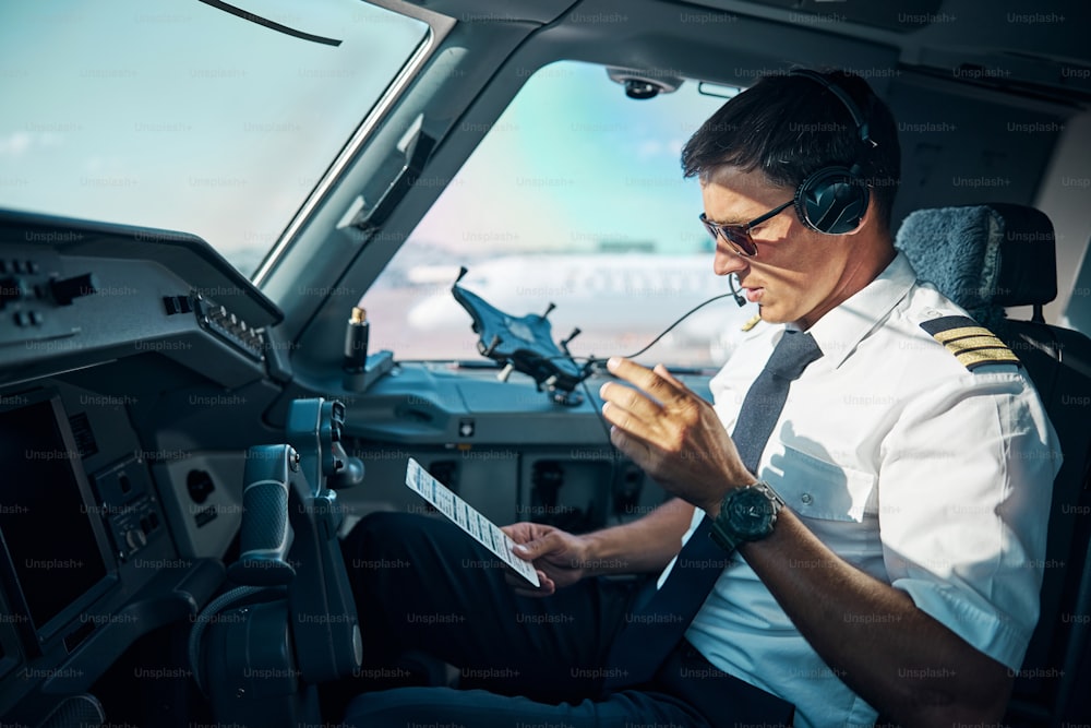 Il giovane professionista maschio con i gadget è seduto al comando nella cabina di pilotaggio e si prepara per il decollo