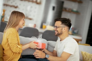 Boyfriend surprising his girlfriend with a gift. Young man giving gift box to his wife