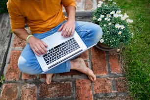 Vista superior de un hombre irreconocible con una computadora portátil que trabaja al aire libre en el jardín, concepto de oficina en casa.
