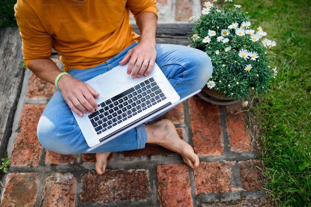 Top view of unrecognizable man with laptop working outdoors in garden, home office concept.