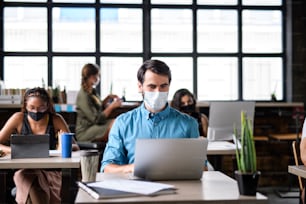 Business people with face masks working indoors in office, back to work after coronavirus lockdown.