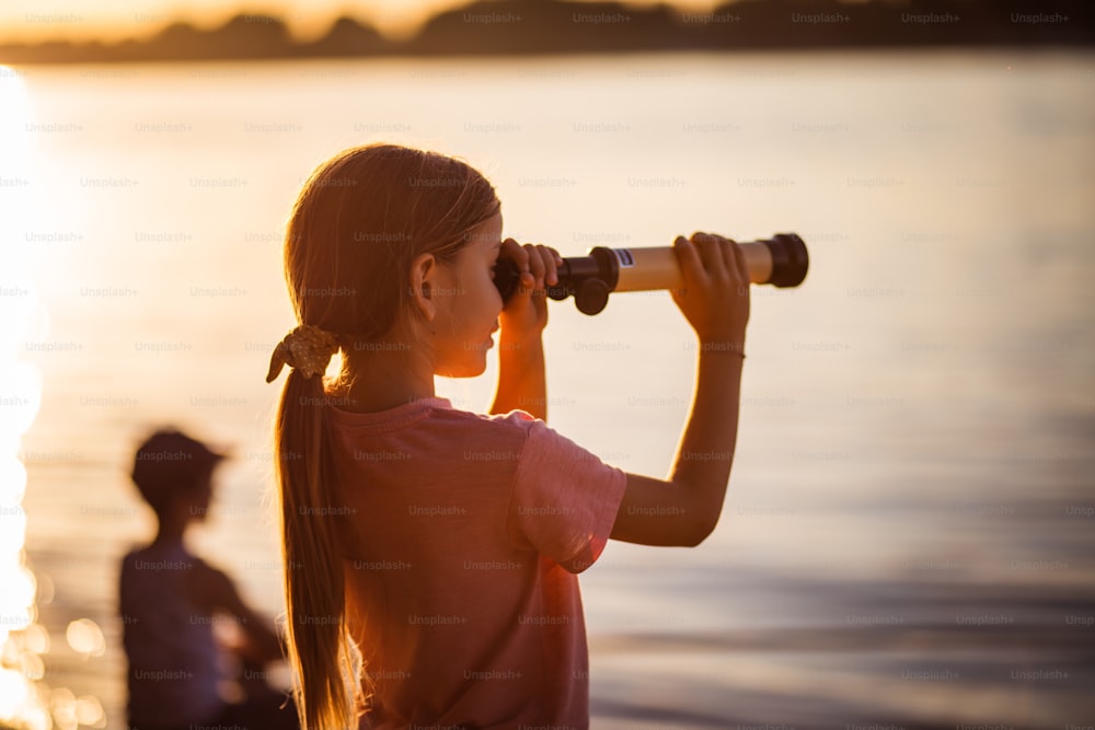 Ce lac est magnifique.  Petite fille regardant à travers le télescope à l’extérieur