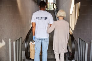 Caregiver and pensioner standing in front of an escalator with their backs to camera