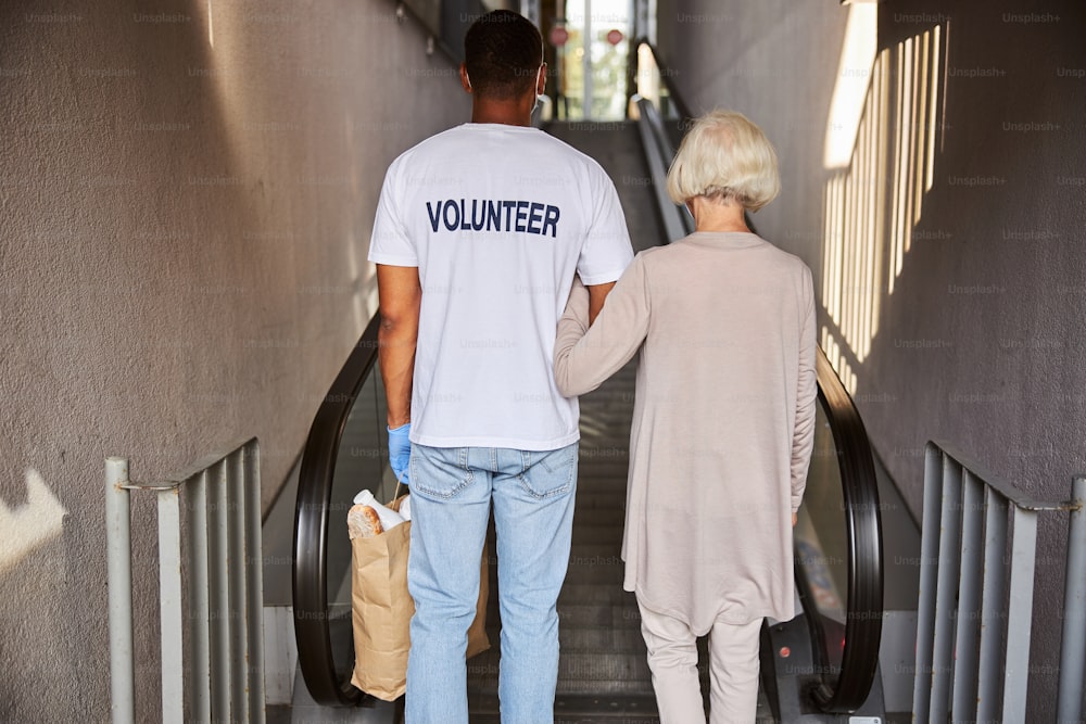 Pfleger und Rentner stehen mit dem Rücken zur Kamera vor einer Rolltreppe