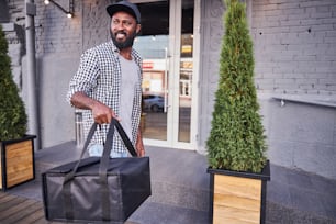Handsome Afro American man looking away and smiling while holding insulated thermal packing bag