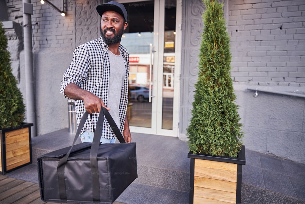 Handsome Afro American man looking away and smiling while holding insulated thermal packing bag