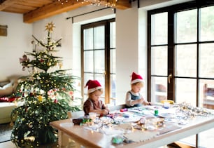 Portrait of happy small girl and boy indoors at home at Christmas, painting pictures.