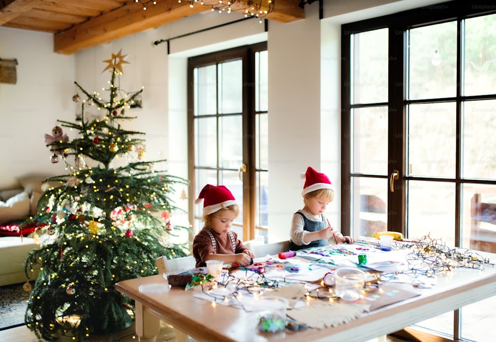 Portrait of happy small girl and boy indoors at home at Christmas, painting pictures.