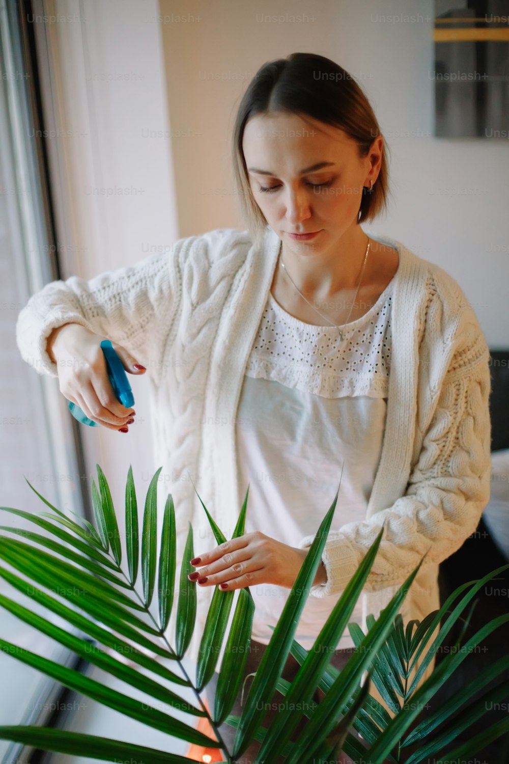 Caucasian woman pouring water from sprinkler on green home plant. Large houseplant howea palm in apartment  house interior indoor. Person care about environment. Hobby leisure.