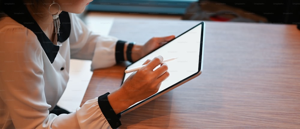 Ausschnittaufnahme einer jungen Frau, die mit einem nachgebauten Tablet-Computer im Büro an ihrem Projekt arbeitet.