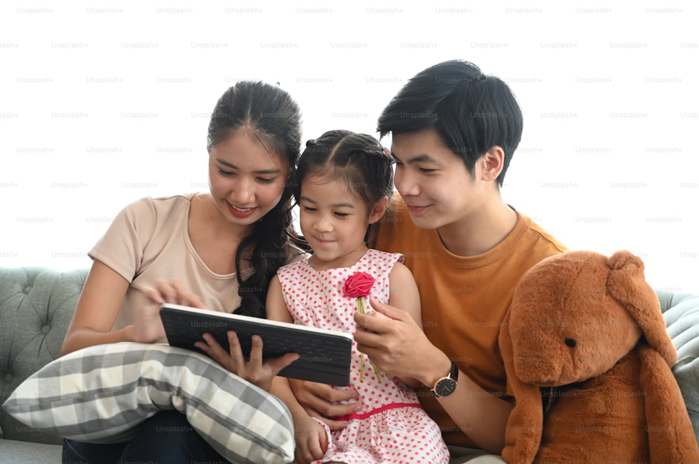 Happy young parents sit on couch with little children have fun using digital tablet together at home.