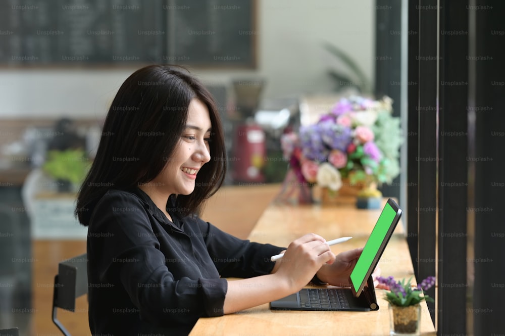 Seitenansicht einer Büroangestellten bei der Arbeit an einem digitalen Tablet mit Greenscreen auf einem Holzschreibtisch.