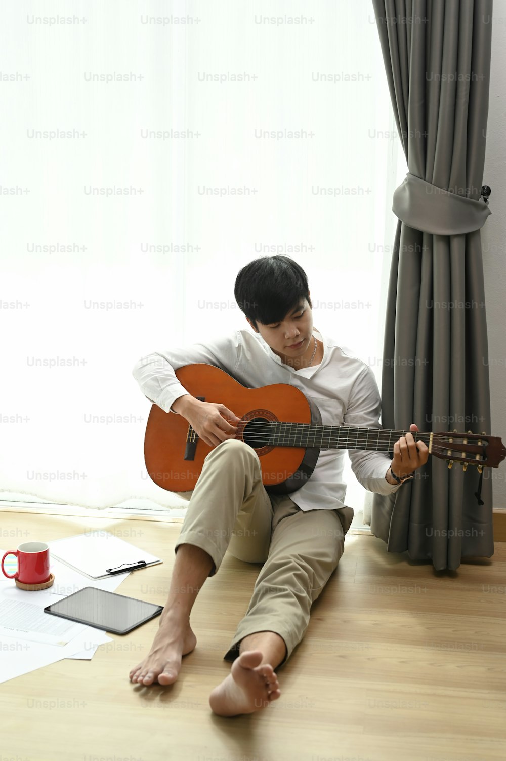 Portrait of young man playing acoustic guitar on floor in living room.