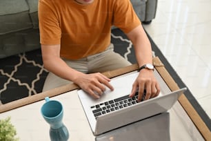 Ausschnittaufnahme eines jungen Mannes mit Laptop im Wohnzimmer zu Hause.