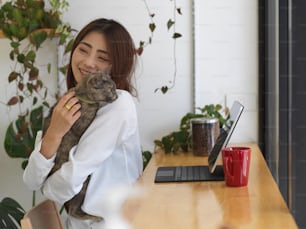 Young adorable female hugging her cat while working at home, work from home concept