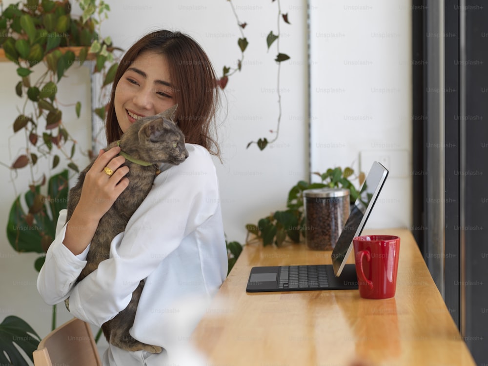 Young adorable female hugging her cat while working at home, work from home concept