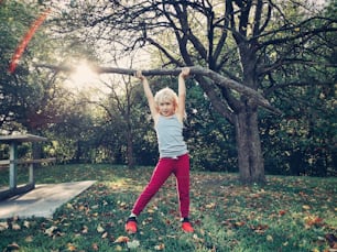 Sporty healthy strong young girl lifting wooden stick branch log in park. Cute kid playing outdoor on summer autumn fall day. Powerful female child girl lifting weights outside.