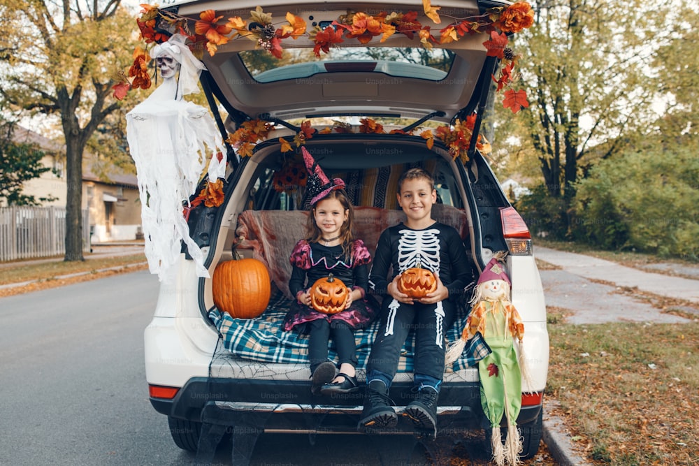 Truque ou tronco. Irmãos irmão e irmã comemorando Halloween no porta-malas do carro. Crianças crianças menino e menina que celebram o feriado de outubro ao ar livre. Distanciamento social e celebração alternativa segura.
