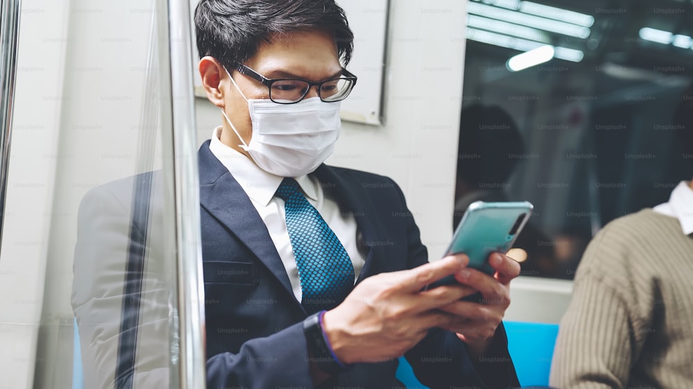 대중 열차에서 휴대 전화를 사용하는 동안 안면 마스크를 착용 한 여행자. 코로나바이러스 질병 또는 COVID 19 전염병 발생 및 러시아워 통근 개념의 도시 도시 생활 방식 문제.
