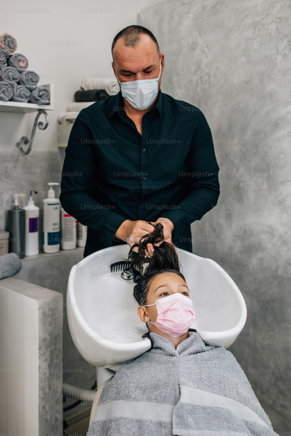 Muchacha joven con máscara facial protectora en el tratamiento de peinado mientras el peluquero profesional se lava suavemente el cabello. Estilo de vida del coronavirus y concepto de nueva normalidad.