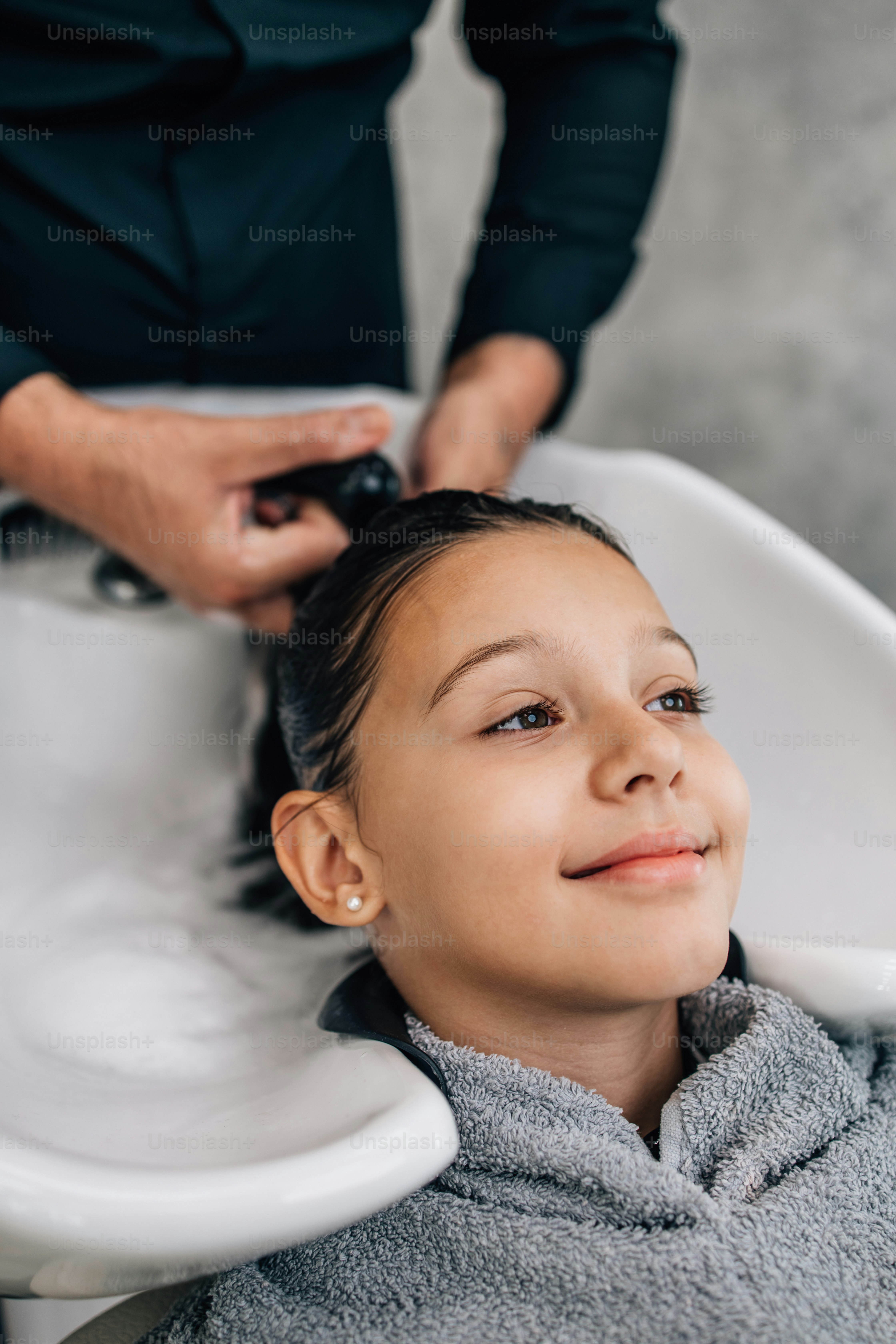 Giovane ragazza al trattamento dell'acconciatura mentre il parrucchiere professionista le lava delicatamente i capelli.