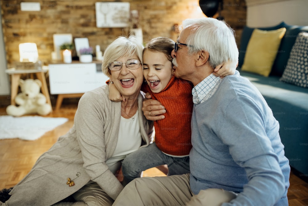 Cheerful little girl having fun and embracing her grandparents at home.