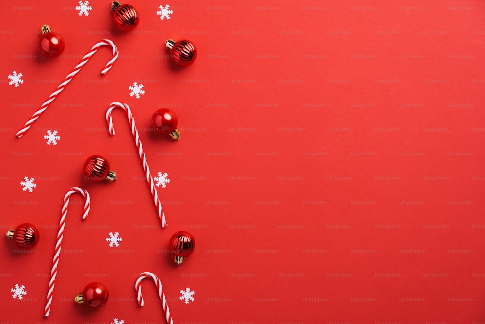 Décoration de boules de Noël rouges, cannes de bonbon, confettis sur fond rouge. Mise à plat, vue de dessus, espace de copie. Maquette de carte de voeux du Nouvel An, modèle de bannière.