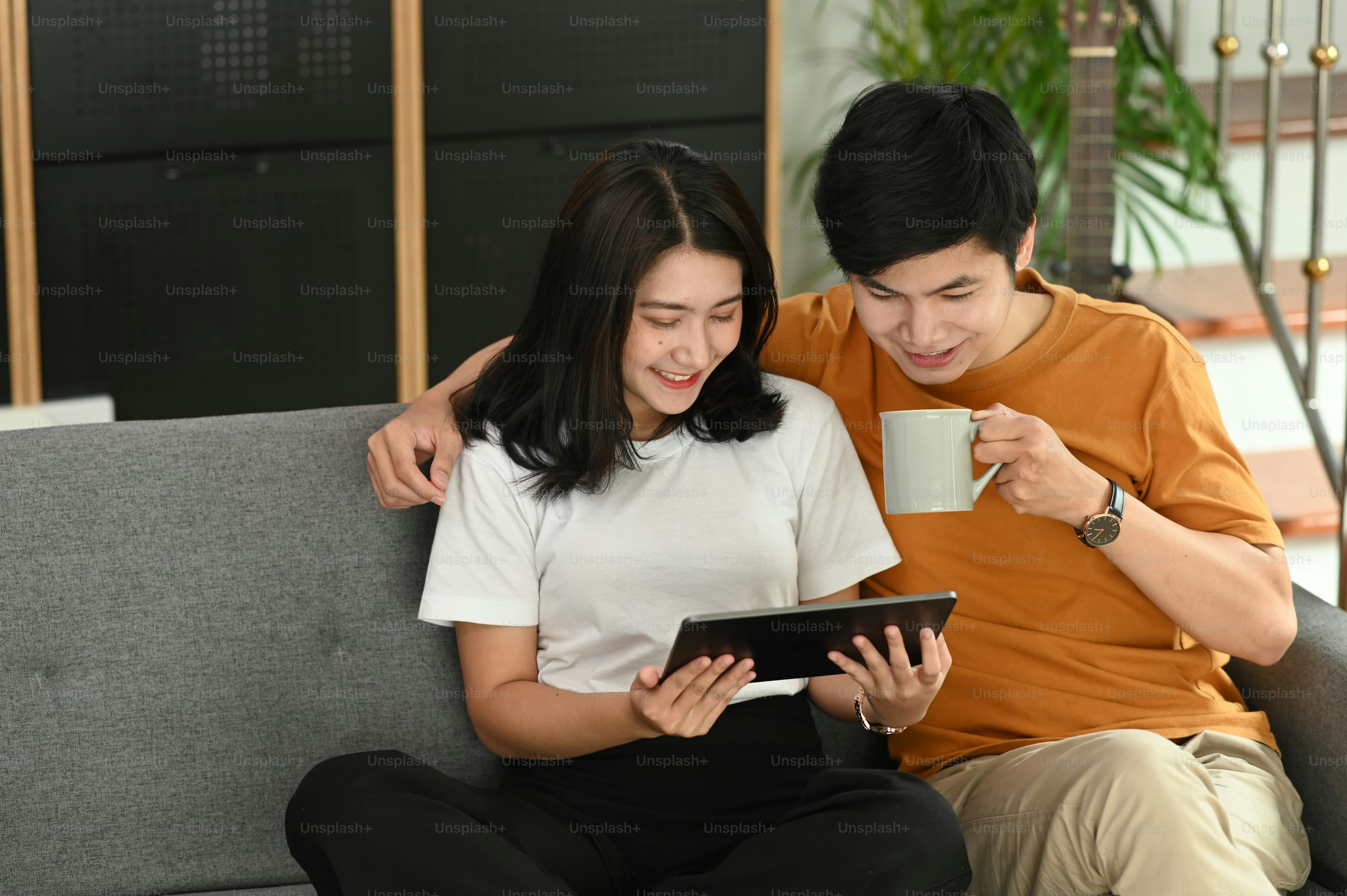 Young smiling couple using digital tablet while sitting on couch at home.