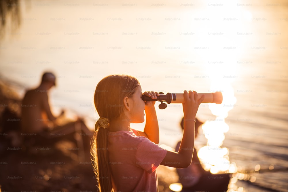 Explore the other side of lake.  Little girl looking through telescope outside