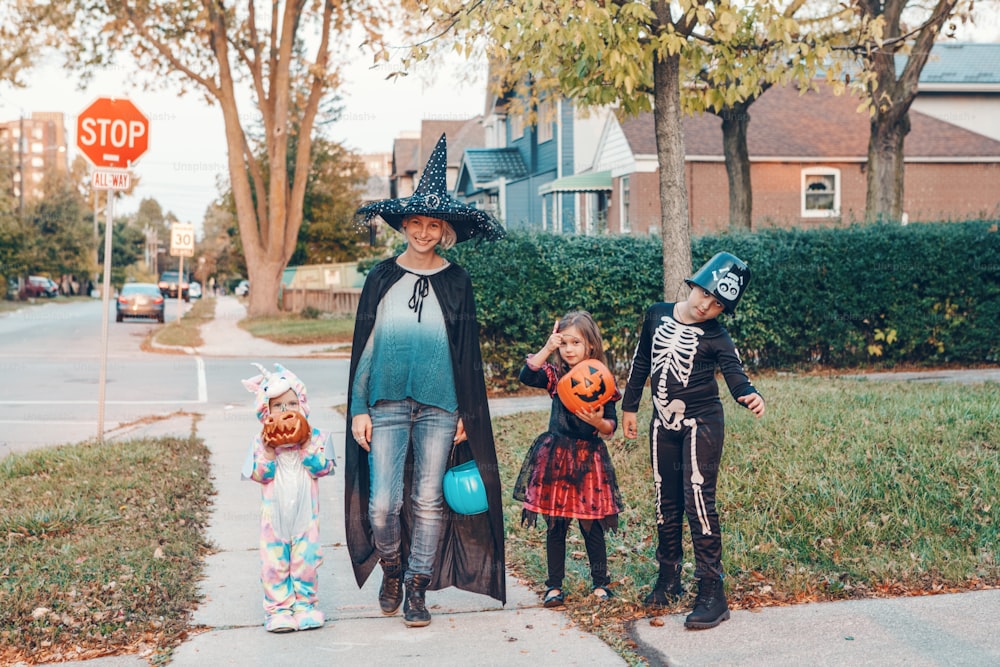 Trick or treat. Mother with children going to trick or treat on Halloween holiday. Mom with kids in party costumes with baskets going to neighbourhood houses for candies, treats.