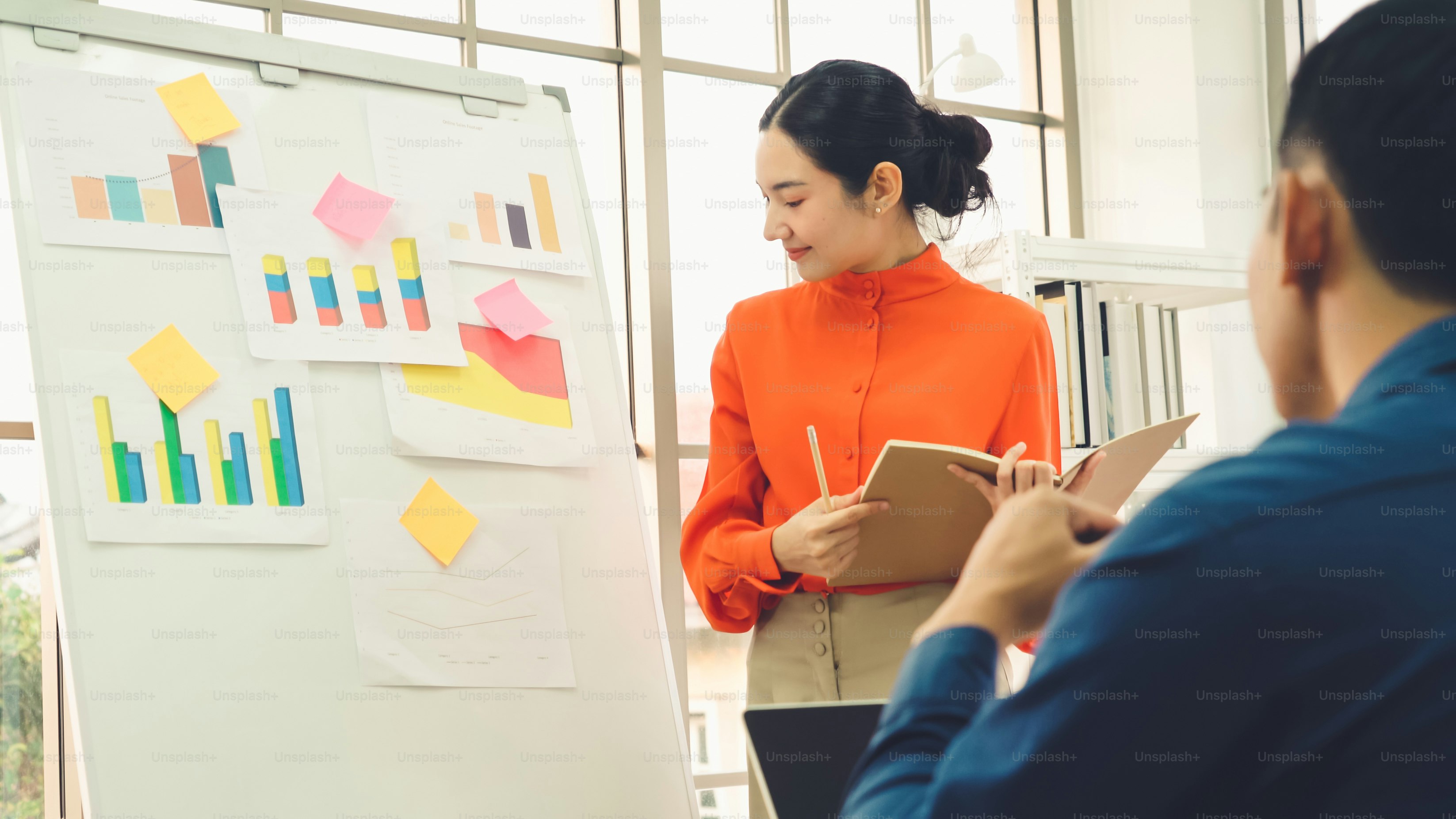 Young woman explains business data on white board in casual office room . The confident Asian businesswoman reports information progress of a business project to partner to determine market strategy .