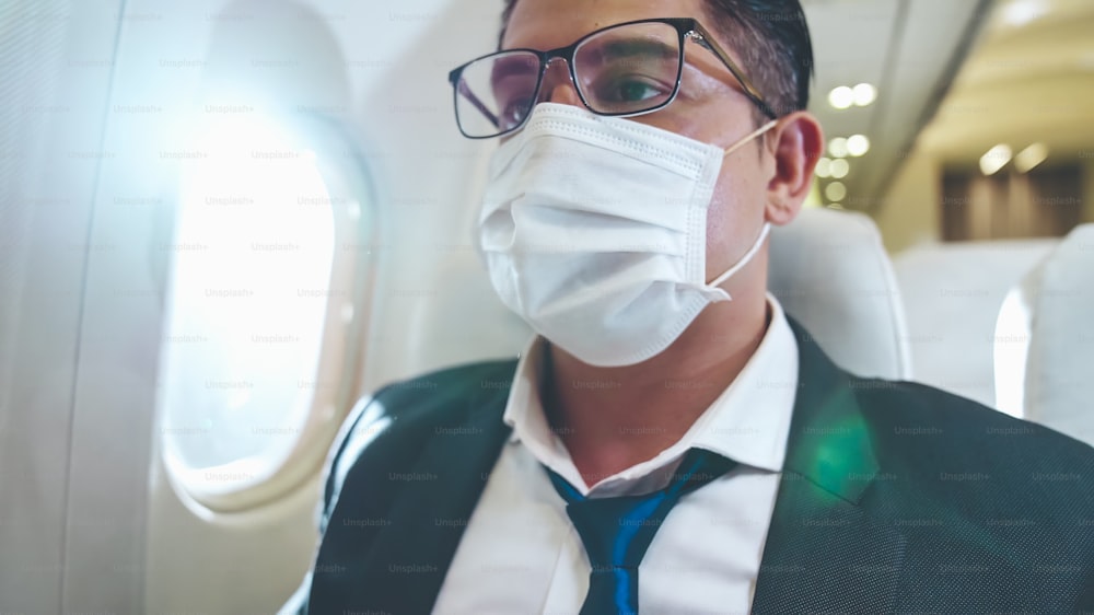 Traveler wearing face mask while traveling on commercial airplane . Concept of coronavirus disease or COVID 19 pandemic outbreak effects on tourism and airline business .