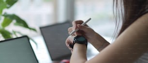 Nahaufnahme einer Frau, die auf einer Armbanduhr schaut, während sie mit digitalen Geräten im Café arbeitet
