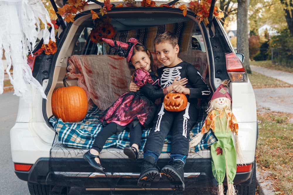 Truque ou tronco. Irmãos irmão e irmã comemorando Halloween no porta-malas do carro. Crianças crianças menino e menina que celebram o feriado de outubro ao ar livre. Distanciamento social e celebração alternativa segura.