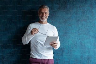 Serious Casual Grey-haired Mature male executive using digital tablet against dark blue background