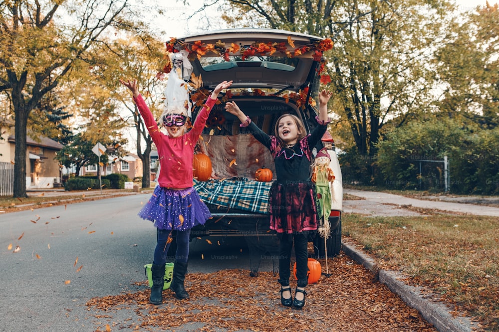 Truque ou tronco. Crianças irmãos irmãs comemorando Halloween no porta-malas do carro. Amigos meninas crianças se preparando para as férias de outubro ao ar livre. Distanciamento social e celebração alternativa segura.