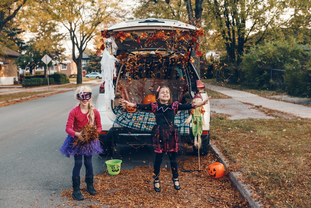 Trick or trunk. Children siblings sisters celebrating Halloween in trunk of car. Friends kids girls preparing for October holiday outdoor. Social distance and safe alternative celebration.