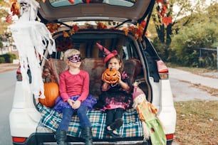 Trick ou tronc. Enfants, frères et sœurs, célébrant Halloween dans le coffre de la voiture. Amis, enfants, filles, se préparant pour les vacances d’octobre en plein air. Distanciation sociale et célébration alternative en toute sécurité.
