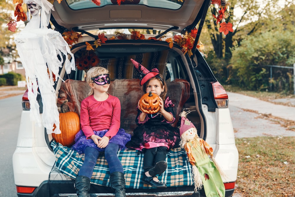 Truco o tronco. Niños, hermanos, hermanas, celebrando Halloween en el maletero del coche. Amigos, niños, niñas, preparándose para las vacaciones de octubre al aire libre. Distanciamiento social y celebración alternativa segura.