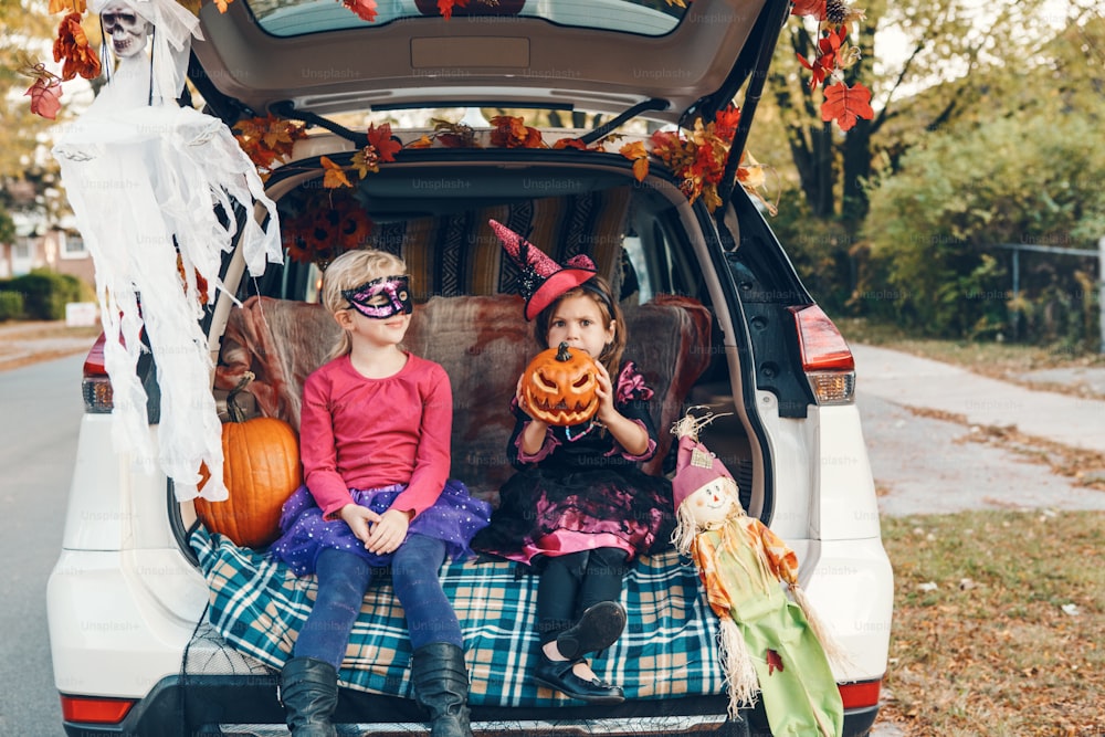 Trick or trunk. Children siblings sisters celebrating Halloween in trunk of car. Friends kids girls preparing for October holiday outdoor. Social distance and safe alternative celebration.