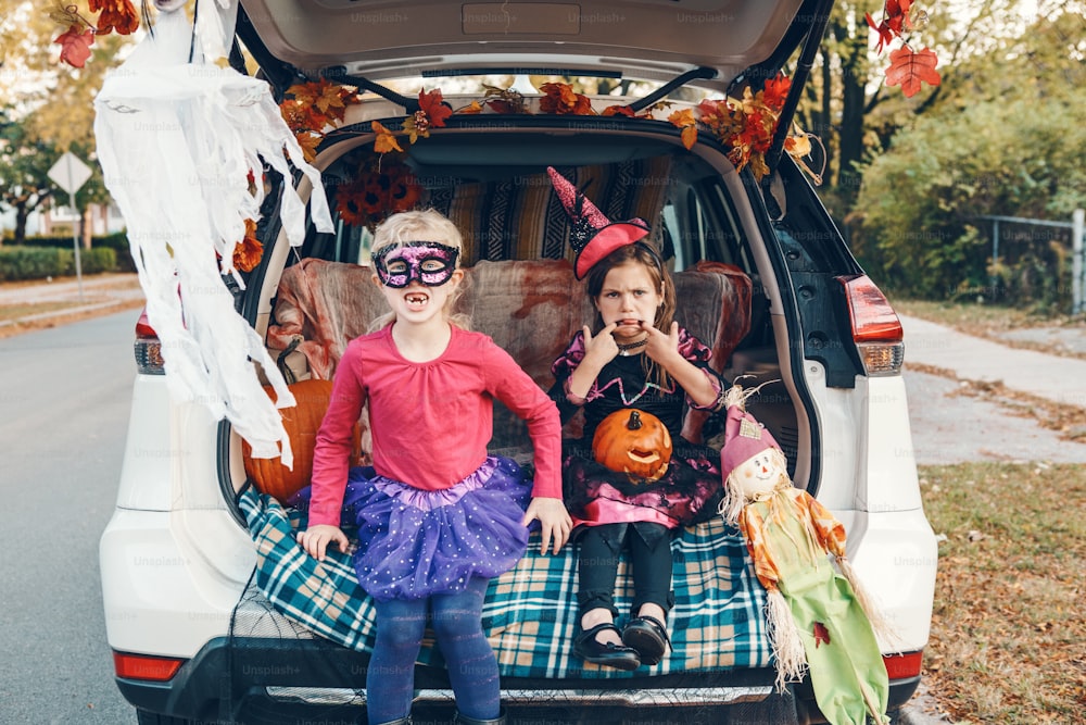 Truque ou tronco. Crianças irmãos irmãs comemorando Halloween no porta-malas do carro. Amigos meninas crianças se preparando para as férias de outubro ao ar livre. Distanciamento social e celebração alternativa segura.