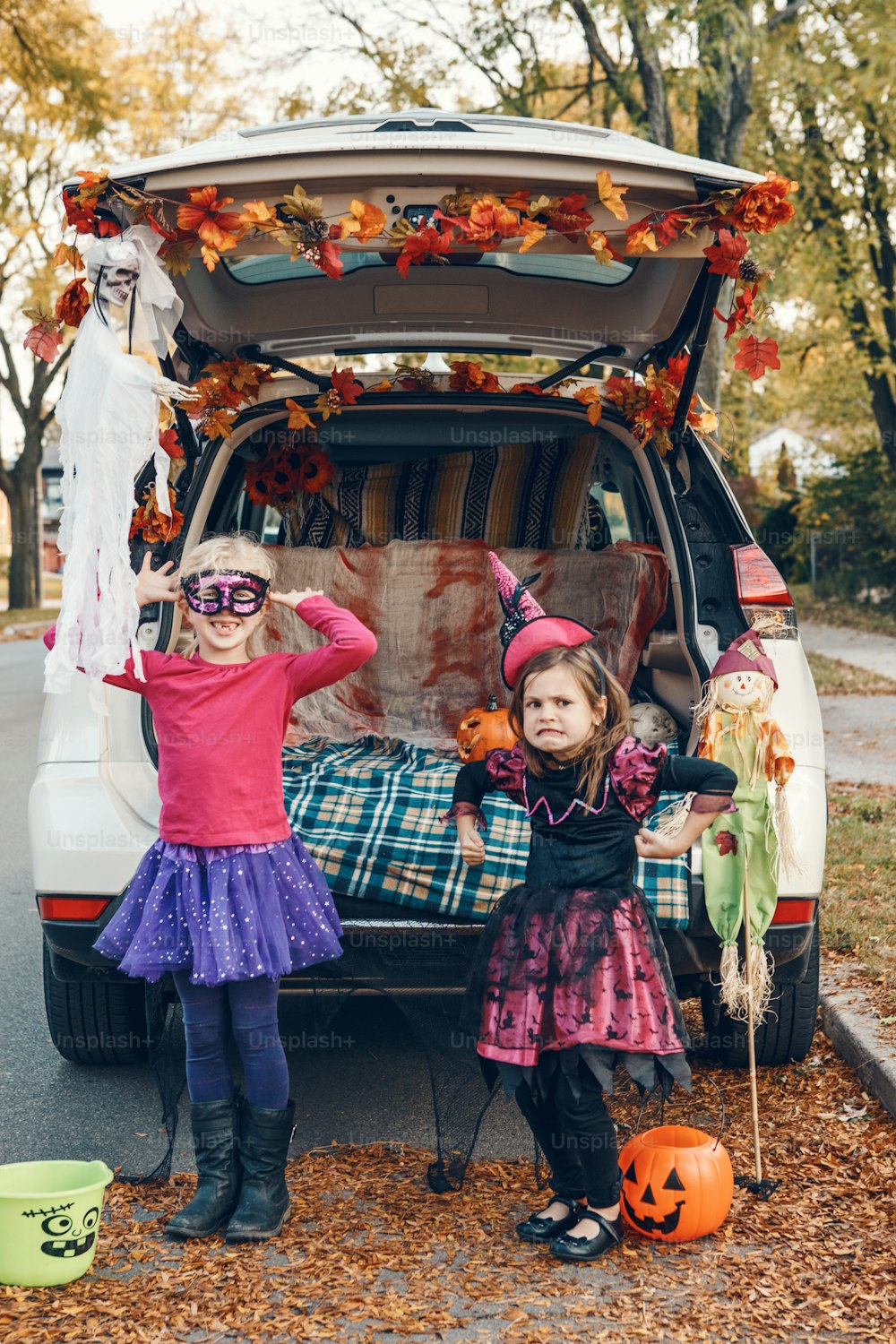 Trick or trunk. Children siblings sisters celebrating Halloween in trunk of car. Friends kids girls preparing for October holiday outdoor. Social distance and safe alternative celebration.