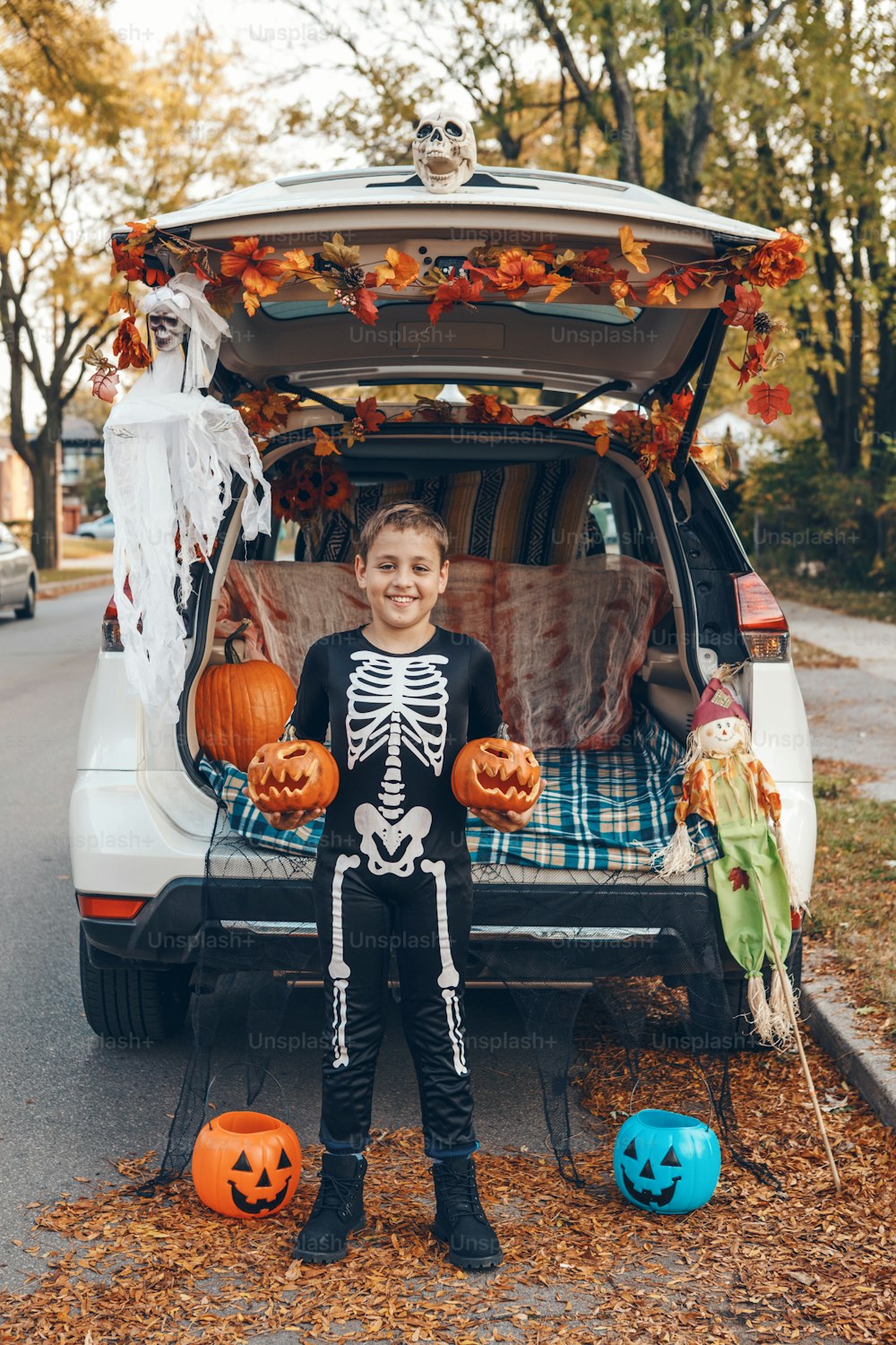 Trick or trunk. Boy child with red carved pumpkins celebrating Halloween in trunk of car. Happy kid preparing for October holiday outdoor. Social distance and safe alternative celebration.