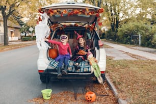 Trick ou tronc. Enfants, frères et sœurs, célébrant Halloween dans le coffre de la voiture. Amis, enfants, filles, se préparant pour les vacances d’octobre en plein air. Distanciation sociale et célébration alternative en toute sécurité.