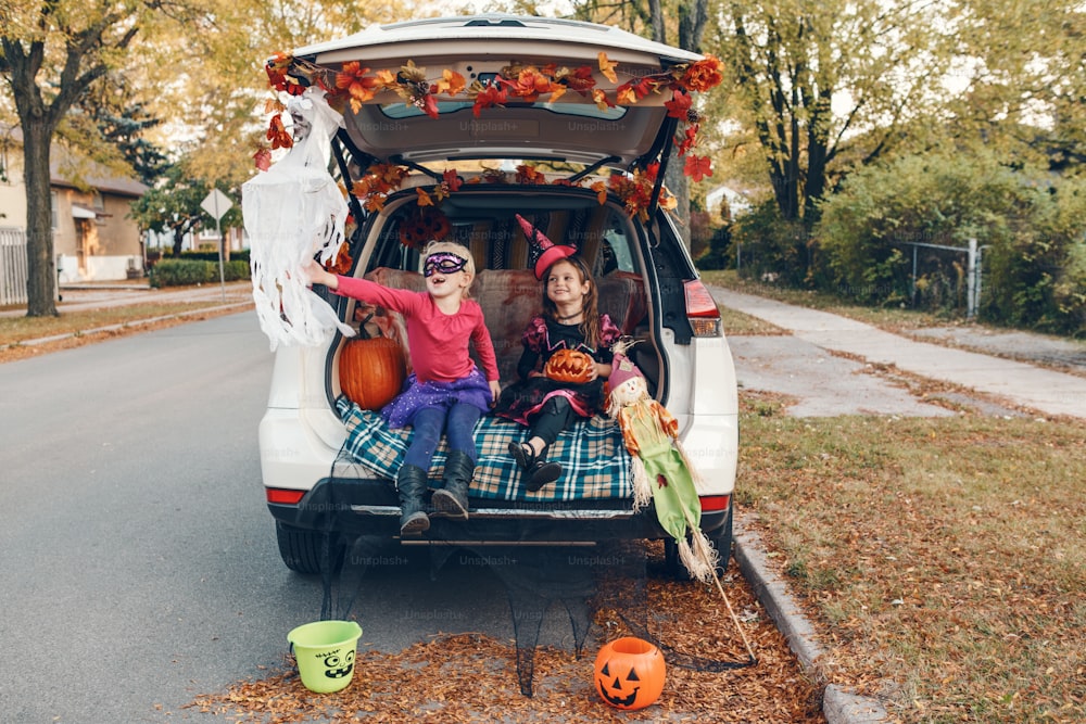 Trick or trunk. Children siblings sisters celebrating Halloween in trunk of car. Friends kids girls preparing for October holiday outdoor. Social distance and safe alternative celebration.