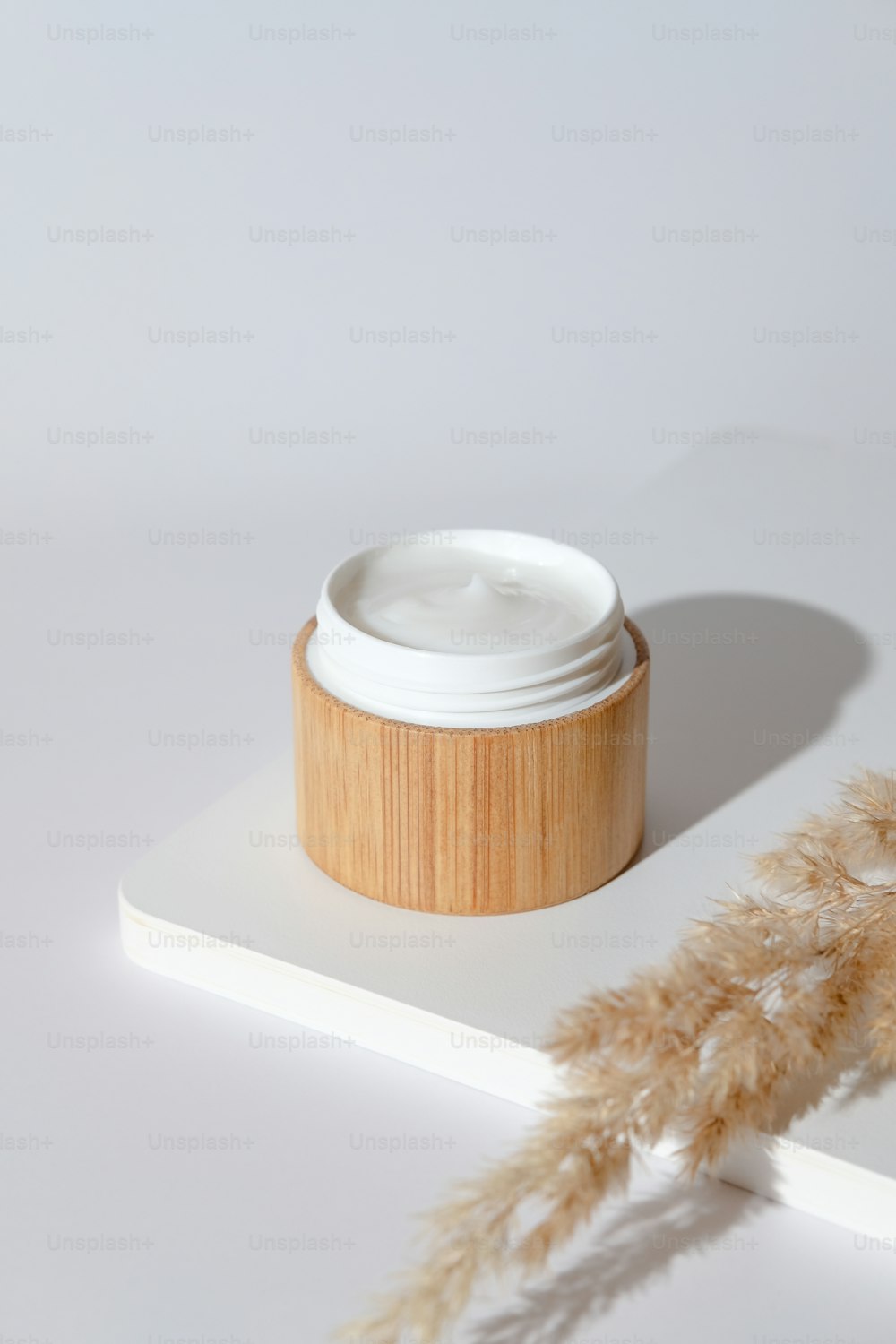 Moisturizing natural cream in bamboo jar and dried flowers on white podium. Organic cosmetics, skincare concept