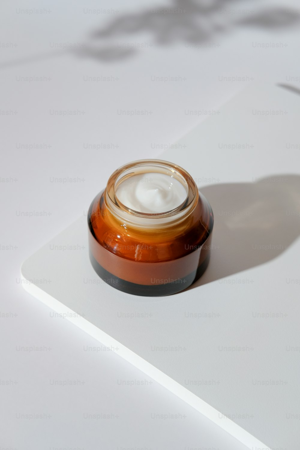Amber glass jar of natural organic moisturizing cream on white podium. Skin care, beauty treatment concept