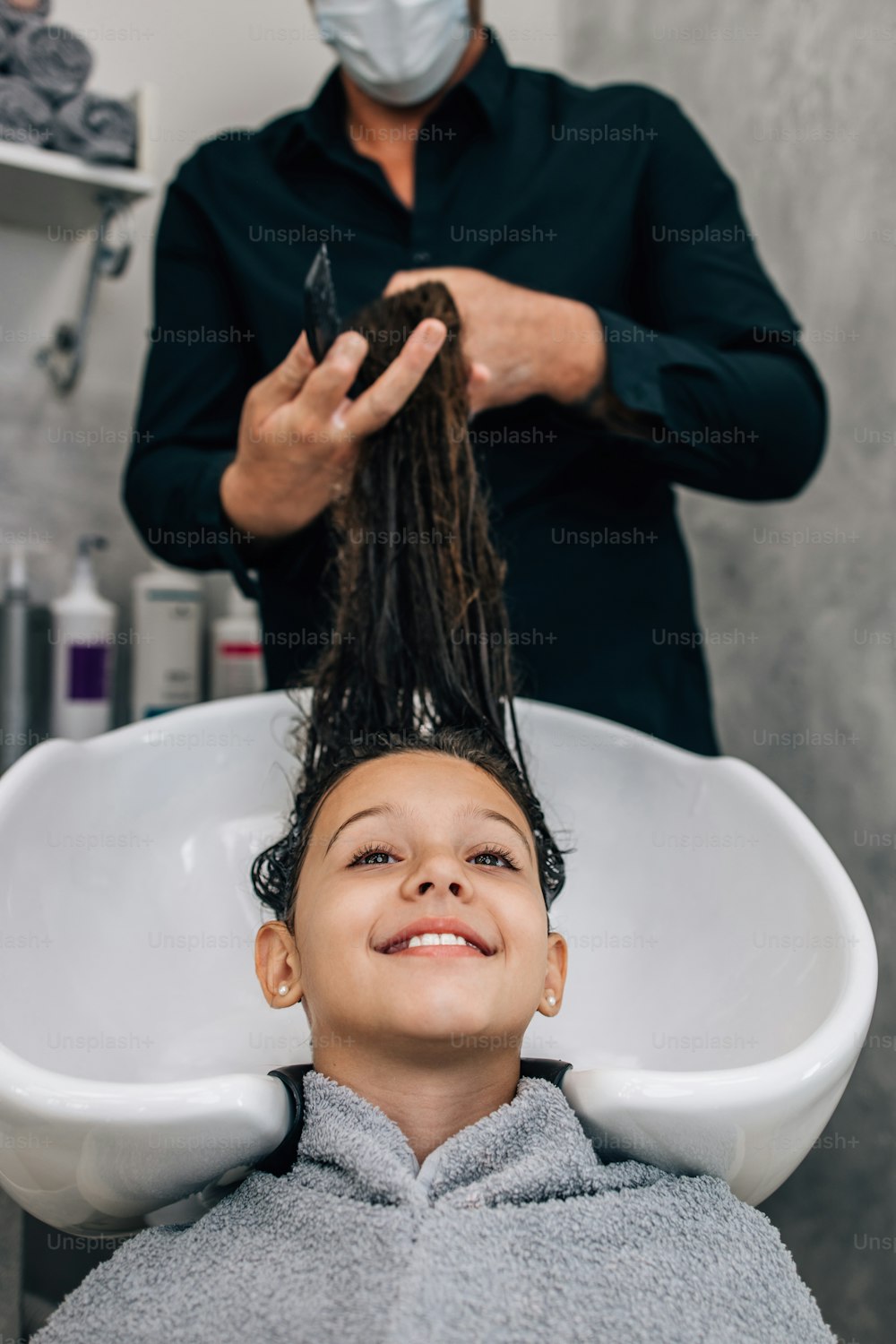 Young girl at hairstyle treatment while professional hairdresser gently washing her hair.